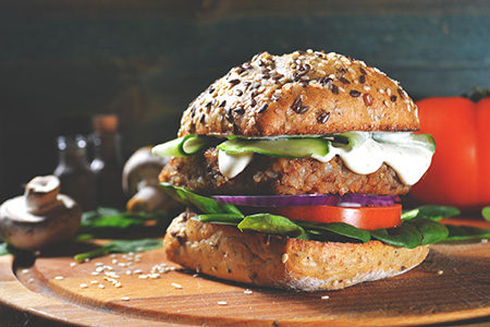 A close-up of a meat analogue burger on a brioche bun with fresh vegetables, featuring a realistic reddish-brown hue created with BioconColors natural colorants like Beetroot or Carmine.