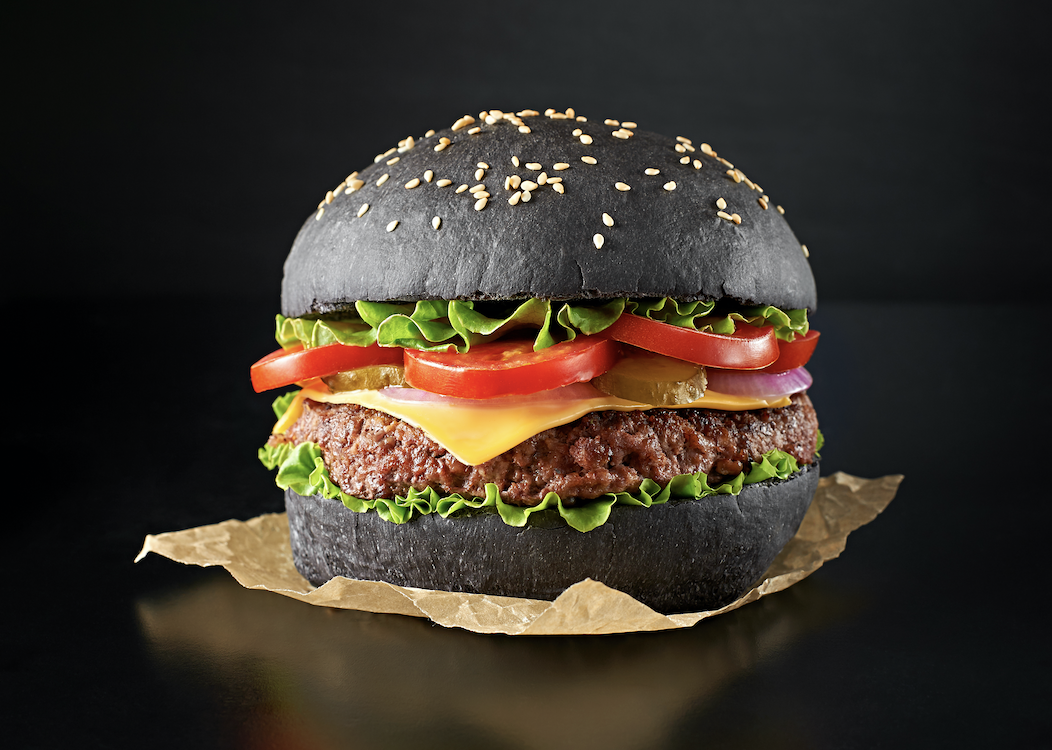 A gourmet burger served on a striking jet-black bun colored with BioconColors vegetable carbon natural colorant, showing a soft texture and intense color stability.